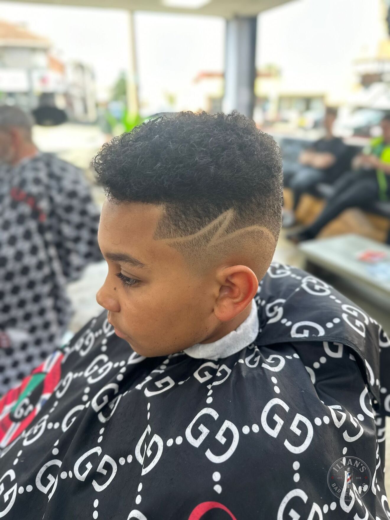 A curly high top with a fade and shaved design at Ilyan's Barber Shop